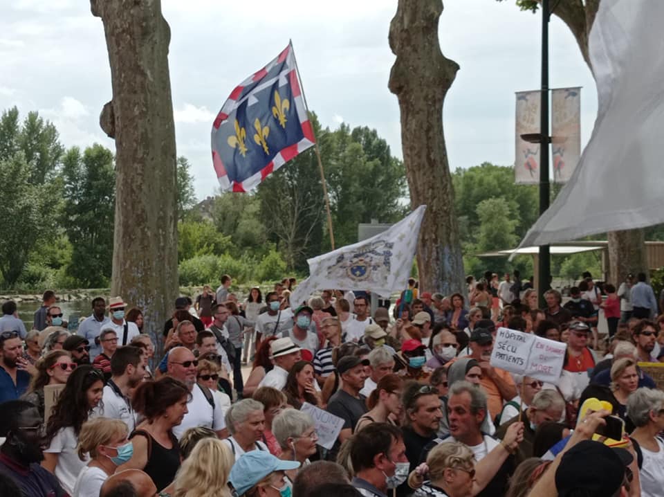 Manifestation contre le pass sanitaire, on peut voir 3 drapeaux, 2 drapeaux royalistes à fleurs de lys et un drapeau blanc.