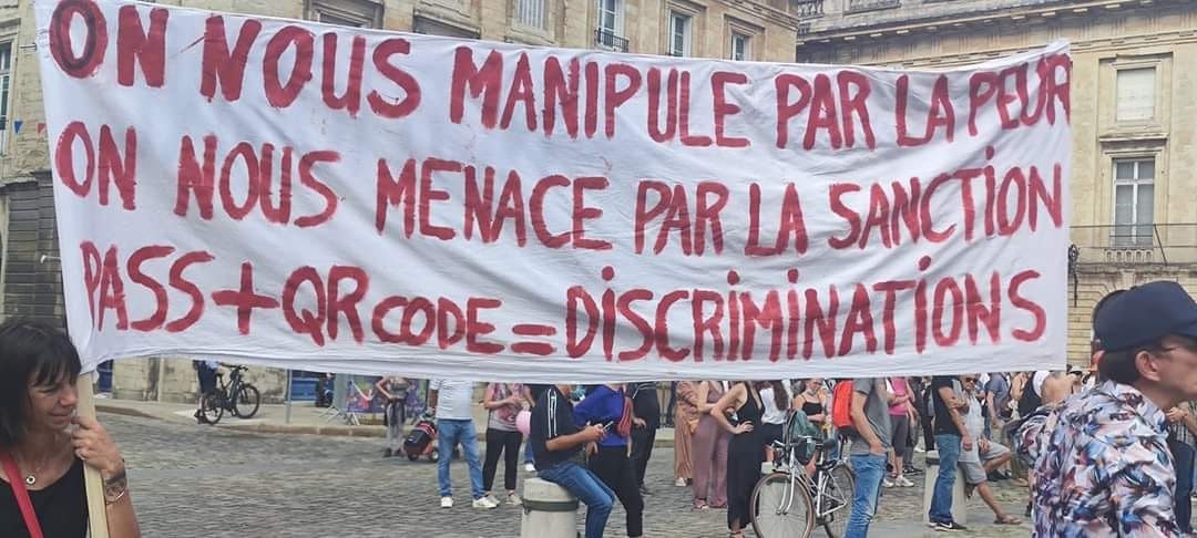Photo d'une banderole complotiste en manifestation "on nous manipule par la peur on nous menace par la santion pass + QRCode = Discriminations"